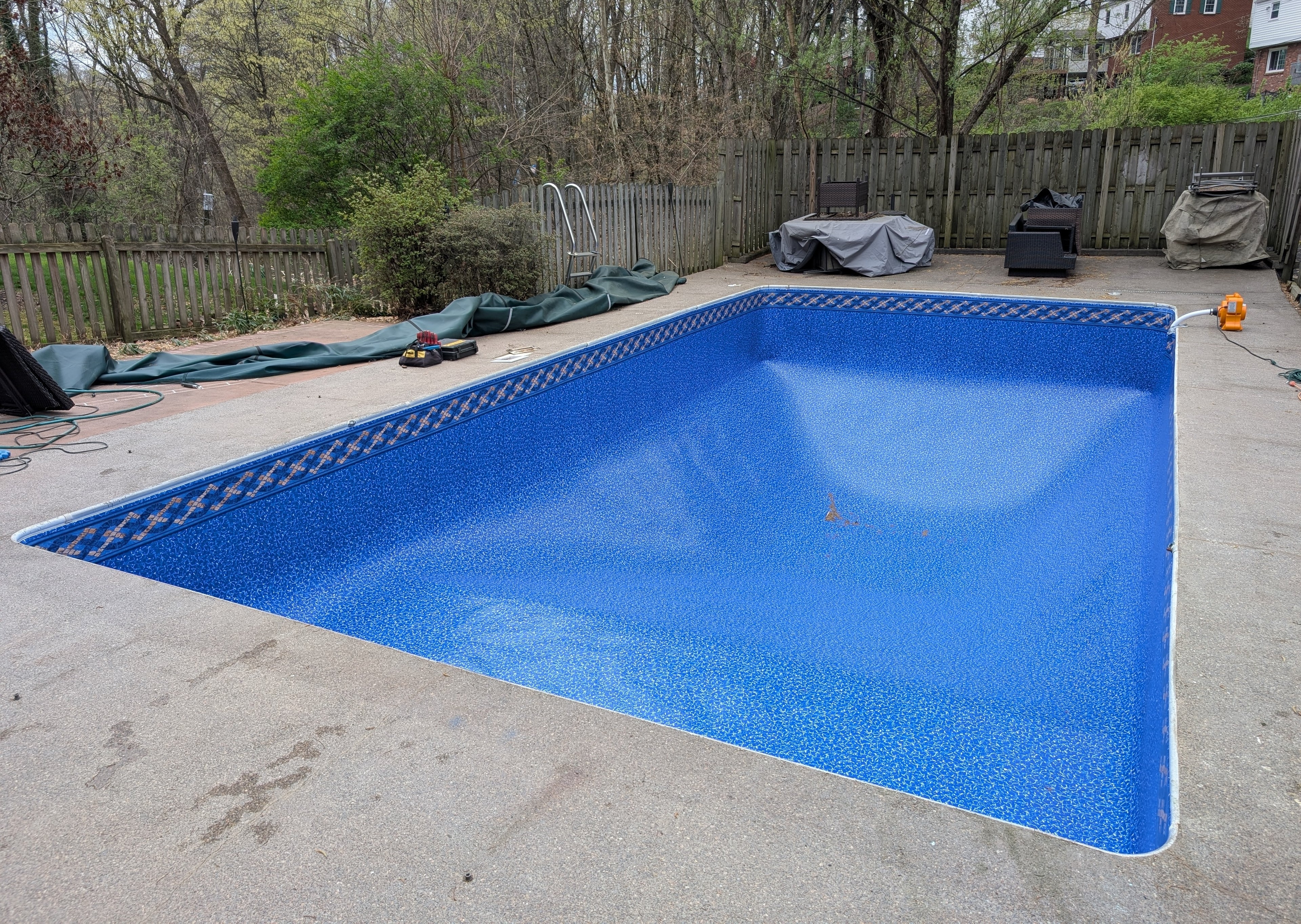 Blue new liner in inground pool in a backyard with trees and a fence in the background.