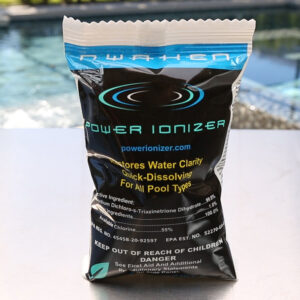 A bag of Awaken Pool Shock by Swimming Pool Discounters, featuring Potassium Monopersulfate for effective pool cleaning, stands upright on a poolside surface with a blurred swimming pool in the background. The packaging is black and blue with yellow and white text.