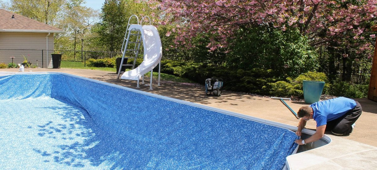 Person cleaning a pool with a slide and playground equipment in the background